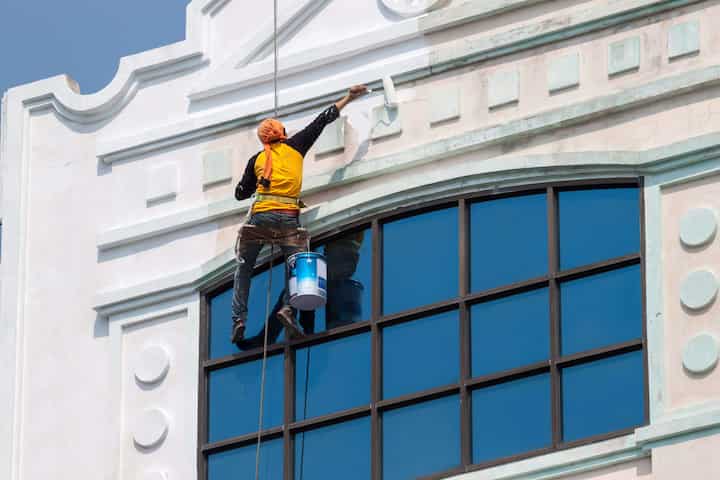 A team of professional painters working on the exterior of a commercial building in Plano, applying fresh coats of paint to revitalize its appearance.