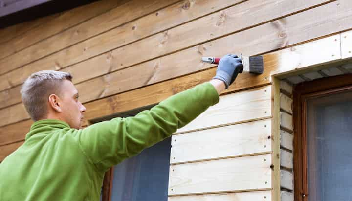 A professional painter using a long-handled brush to apply paint to the exterior of a house in Plano.